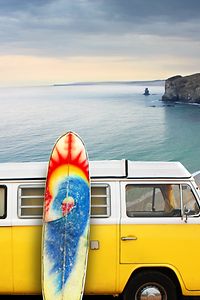 A yellow van with a surf board at the beach